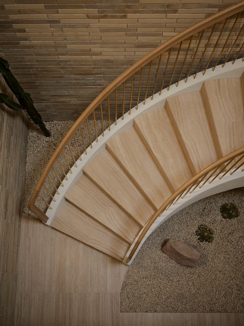 Curved timber staircase seen from above, with a brass balustrade and a gravel garden below