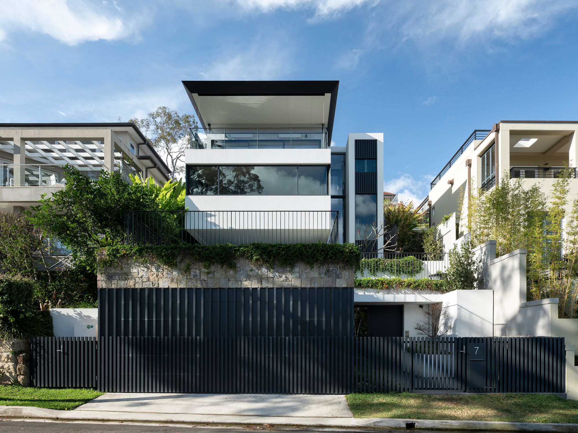 Shellbank House street facade with a black picket fence, sandstone wall and cantilevered upper storey