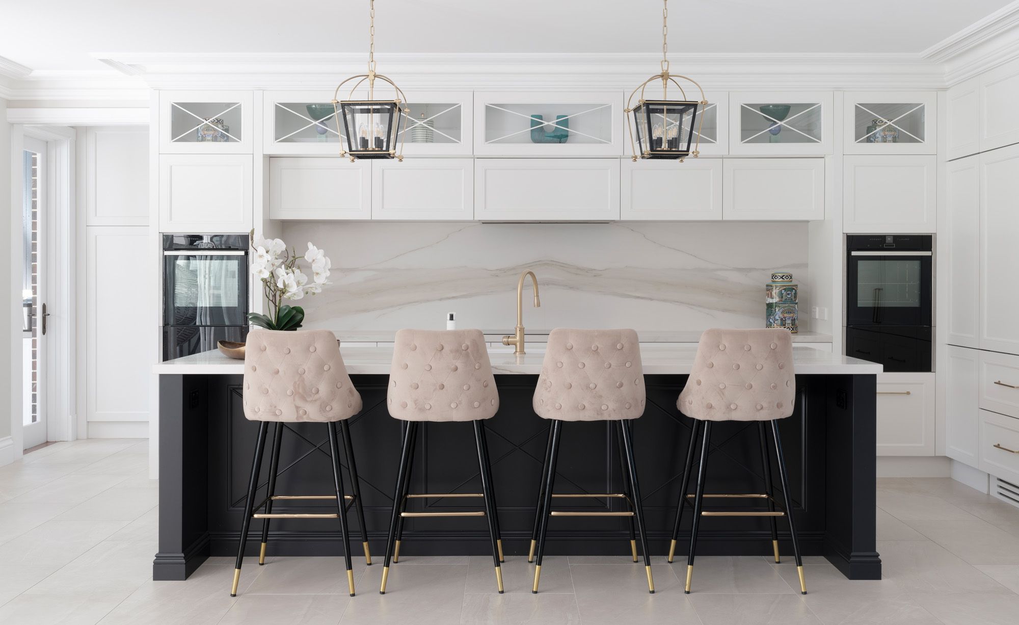 Kitchen with a marble island, upholstered stools and lantern pendants