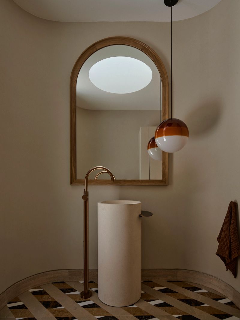 Powder room with a pedestal basin, arched mirror and round skylight