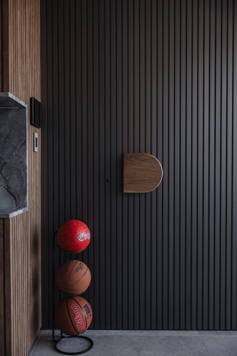 Entry with dark timber battened walls, a round timber handle and basketballs on a stand