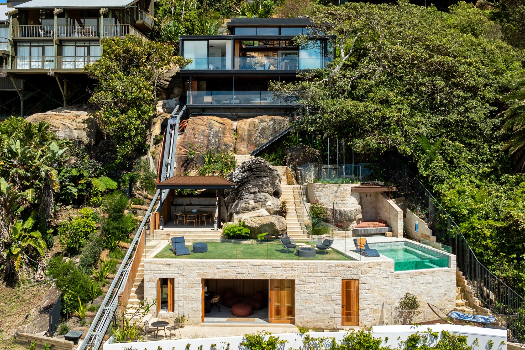 Swell and High Swell stepping down a bush hillside at Palm Beach, glass pavilions above a sandstone pool terrace