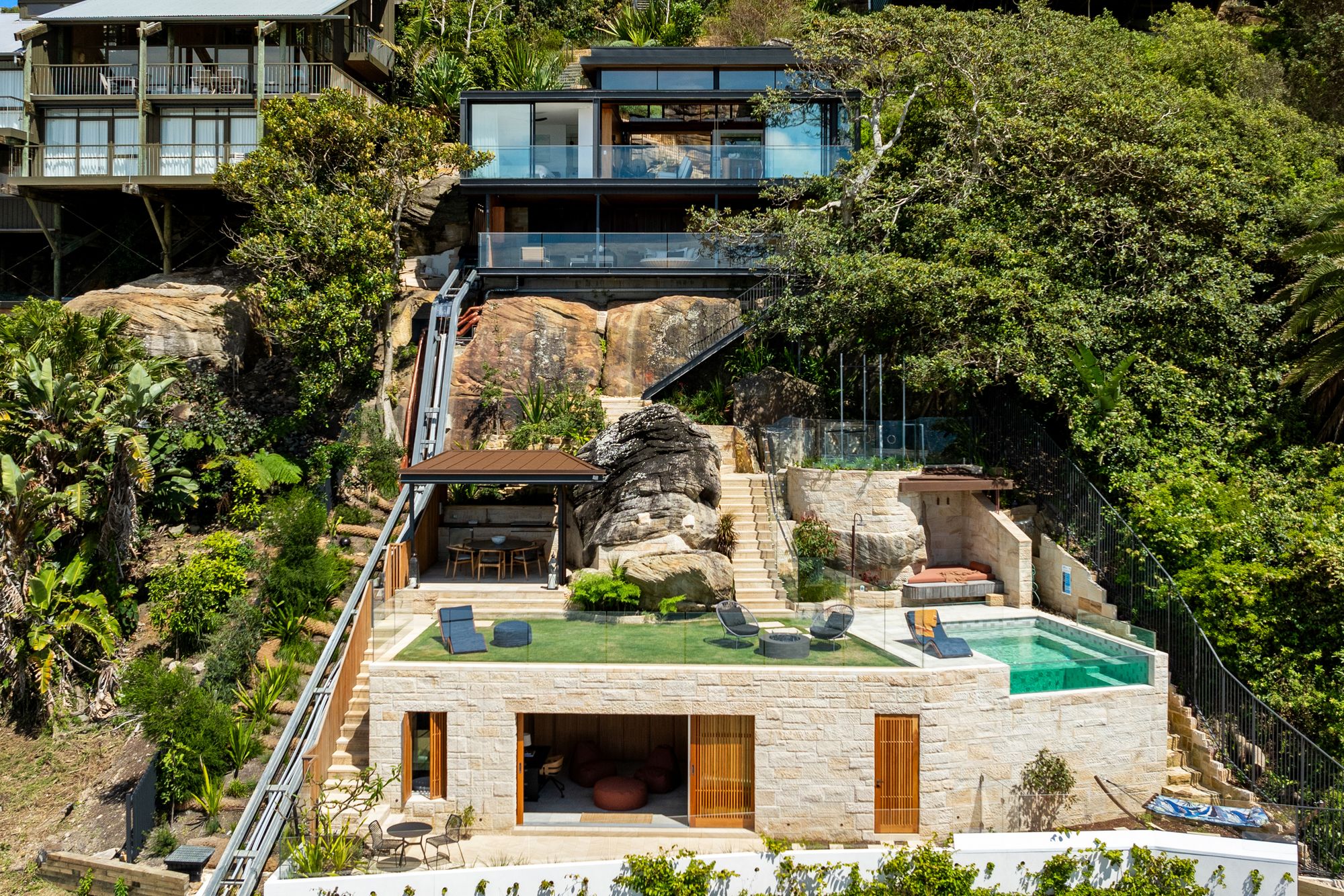 Swell and High Swell stepping down a bush hillside at Palm Beach, glass pavilions above a sandstone pool terrace