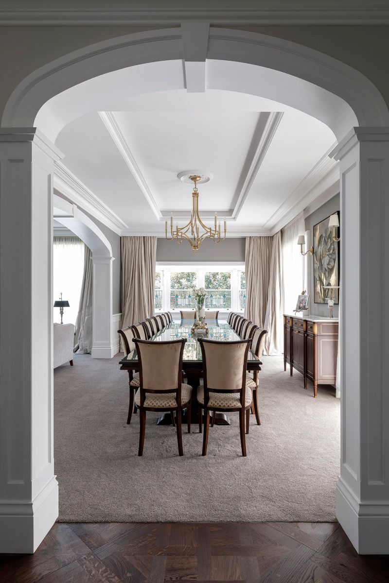 Dining room seen through an arched doorway, with a chandelier and upholstered chairs