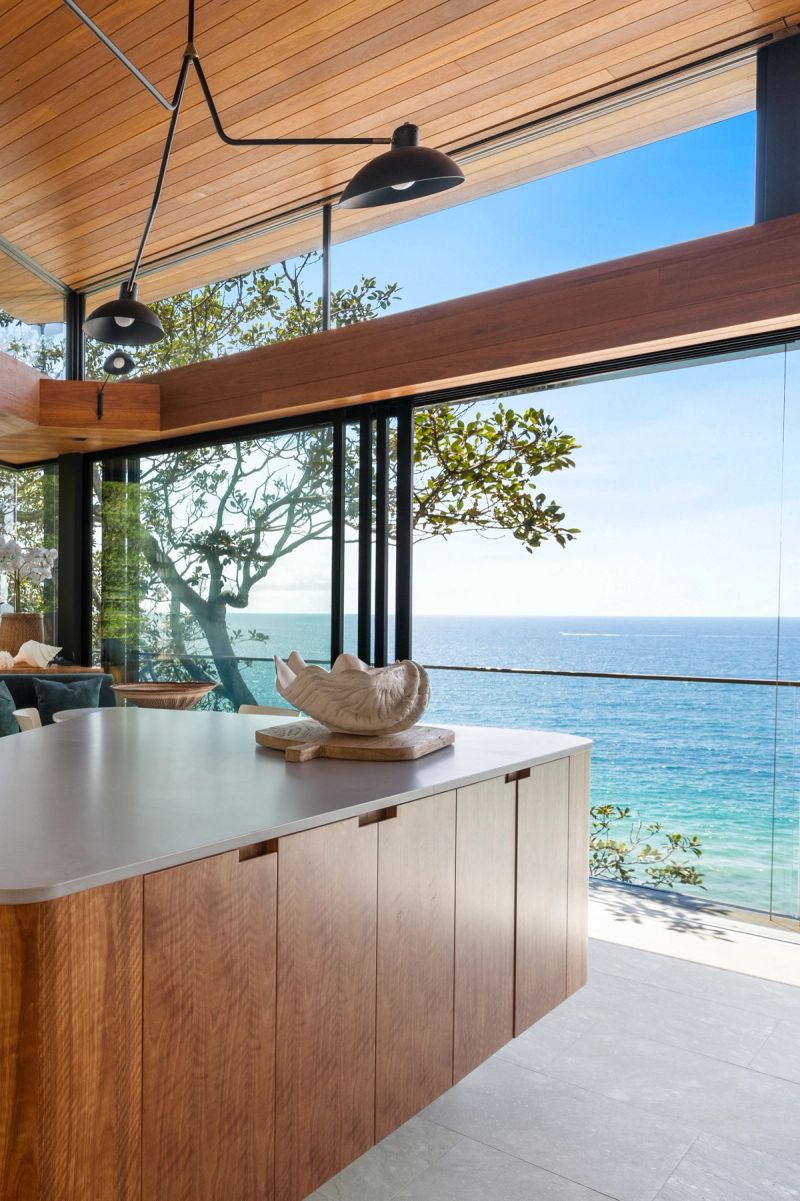 Kitchen island with timber cabinetry and glass walls to the ocean