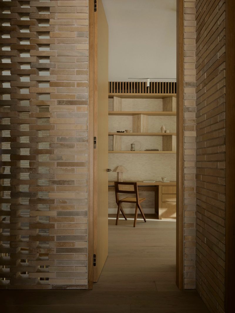 View through a brick doorway into a study with timber shelves and a desk