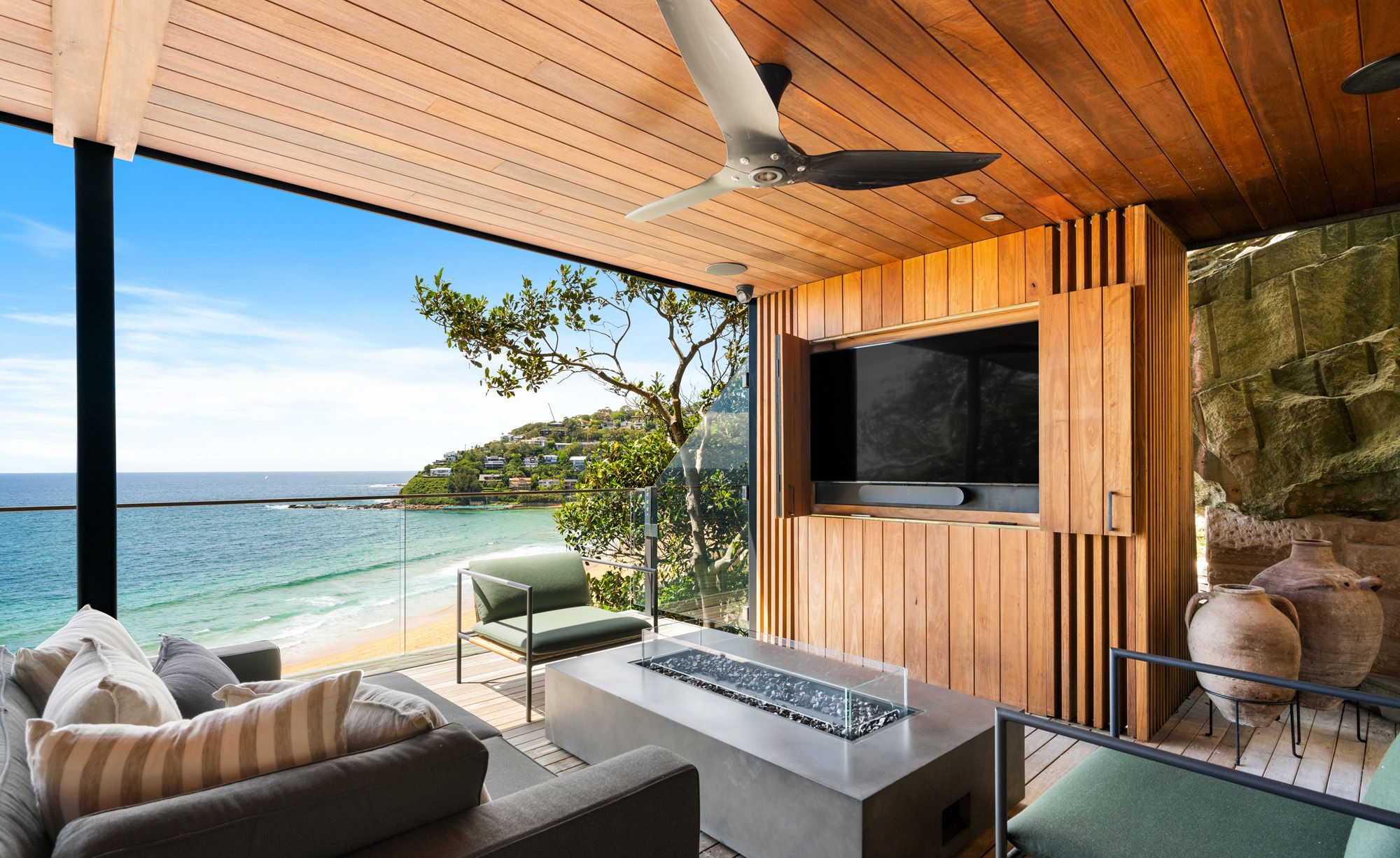 Covered deck with a fire table and lounges, Palm Beach below
