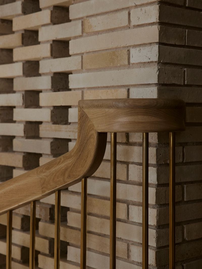 Timber handrail with brass balusters against a pale brick wall