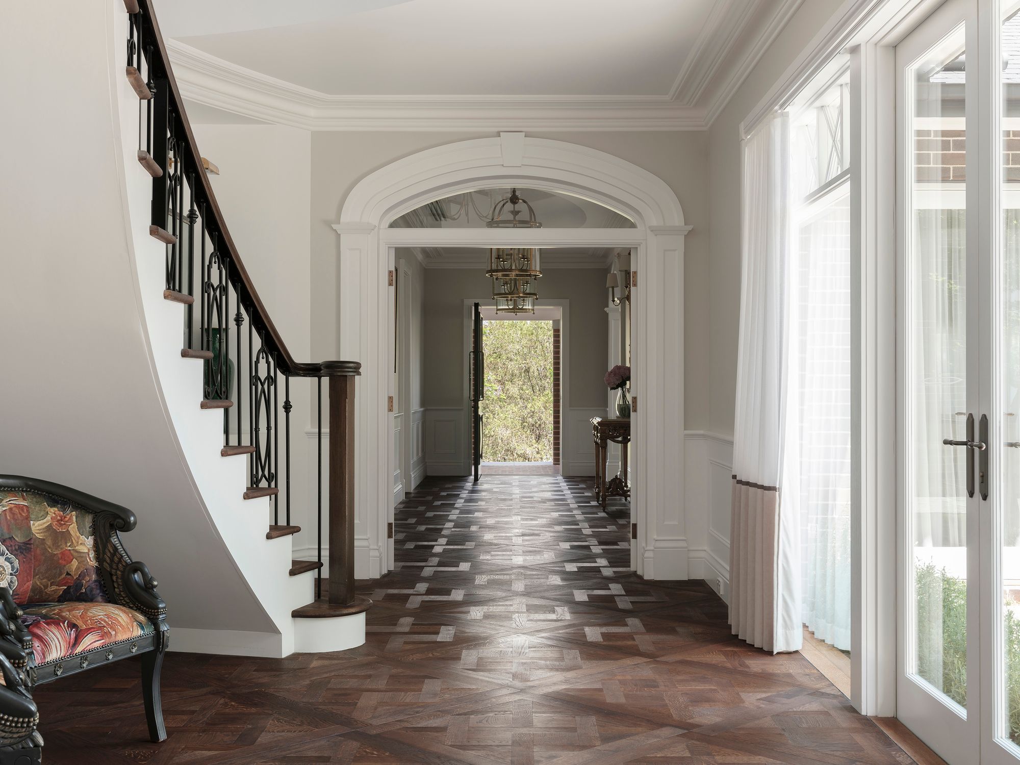 Entry hall at Sussex House with a curved staircase, arched doorway and parquetry floor
