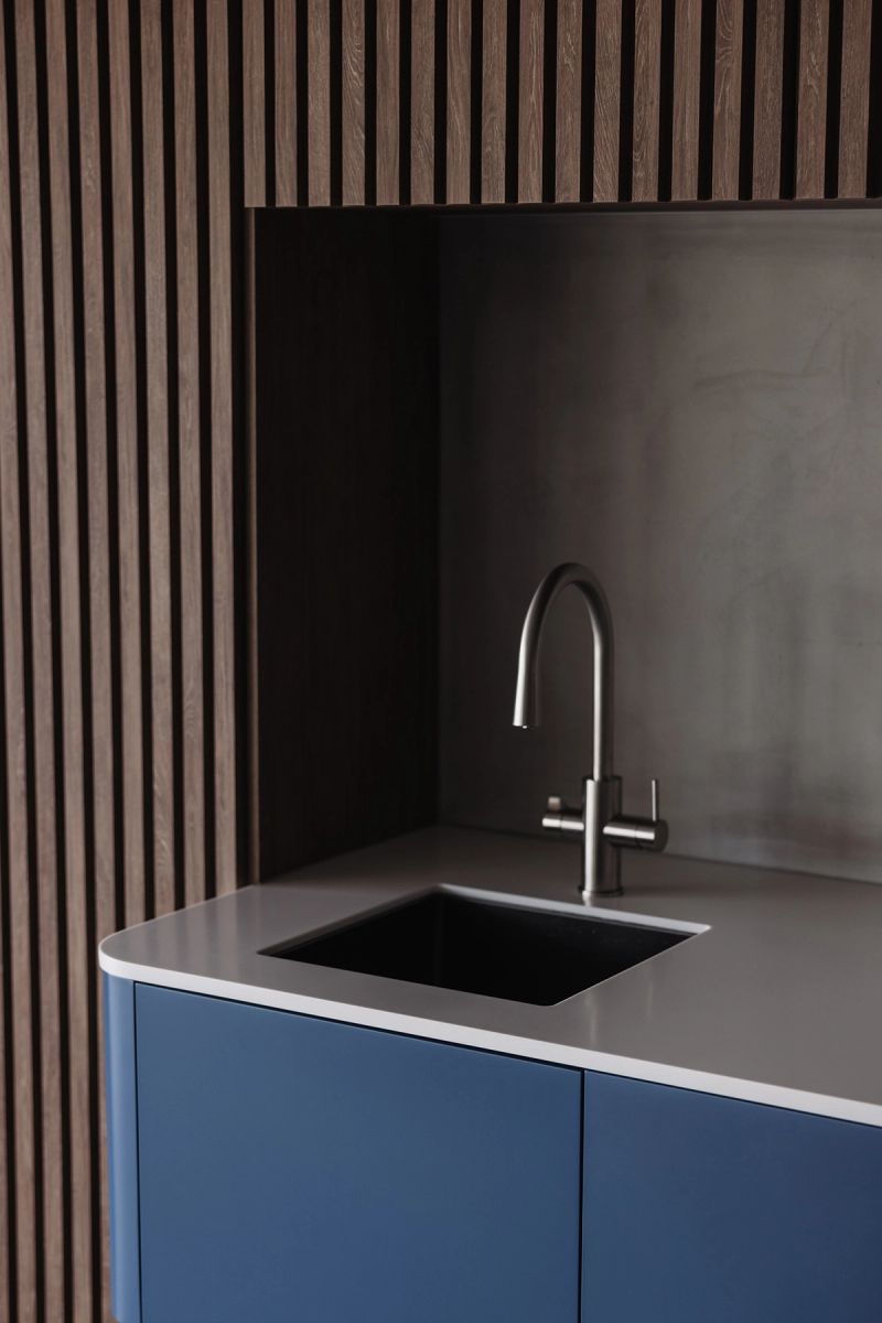 Blue joinery with a stone benchtop and sink beneath timber battens