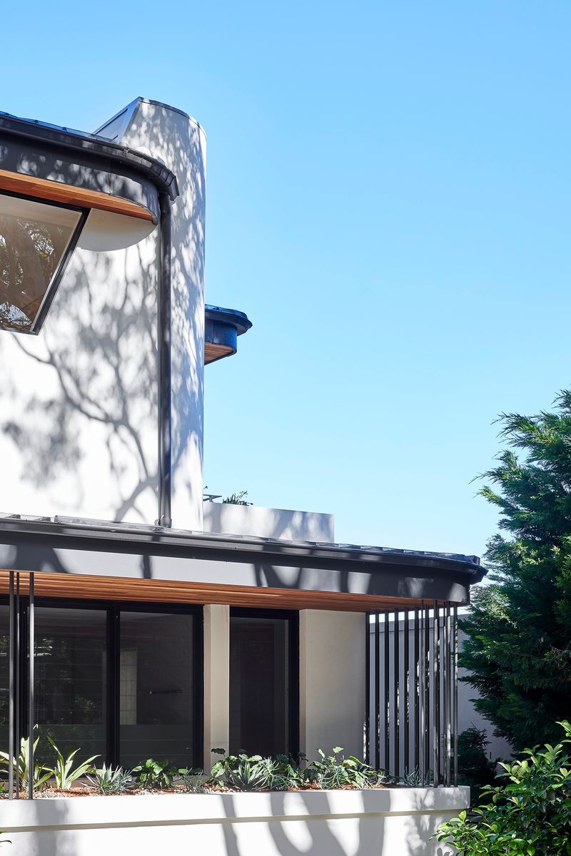 Curved rendered wall and timber clad balcony of Cobbittee House against a blue sky