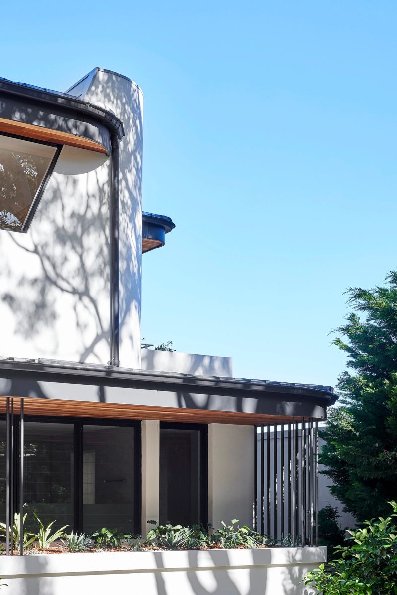 Curved rendered wall and timber clad balcony of Cobbittee House against a blue sky