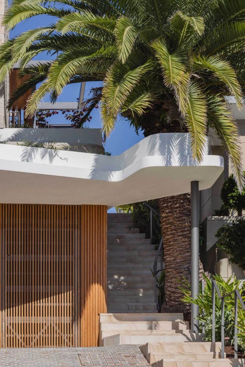 Curved white balcony and timber screened entry stair beneath a palm at Casa Risata