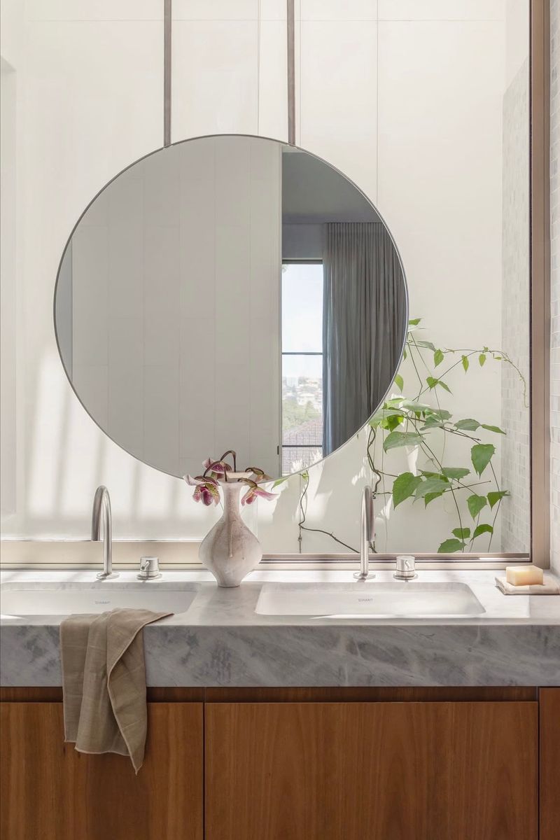Round mirror above a marble vanity with a trailing plant