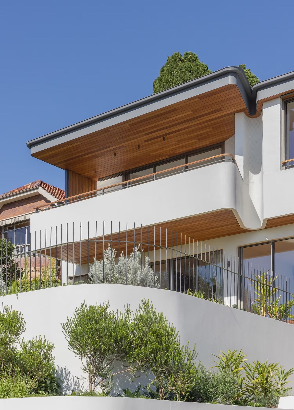 Casa Risata street facade with curved white balconies, timber soffits and olive trees