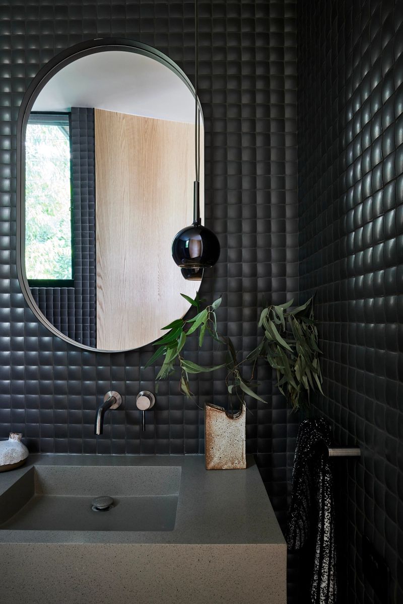 Powder room with black textured tiles, an oval mirror and a stone basin