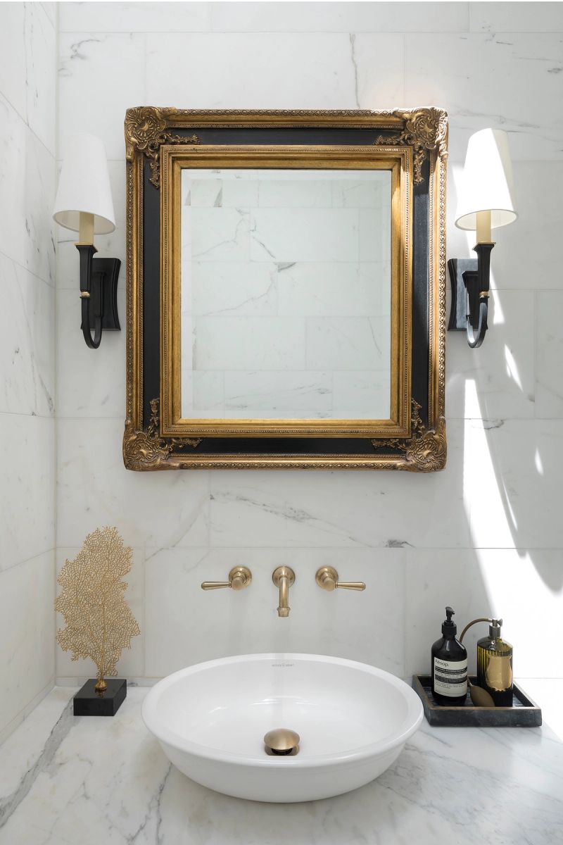 Marble powder room with a gilt framed mirror, wall sconces and a round basin