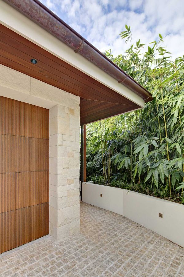 Sandstone and timber entry at Quiet House beneath a copper roof, with bamboo beyond