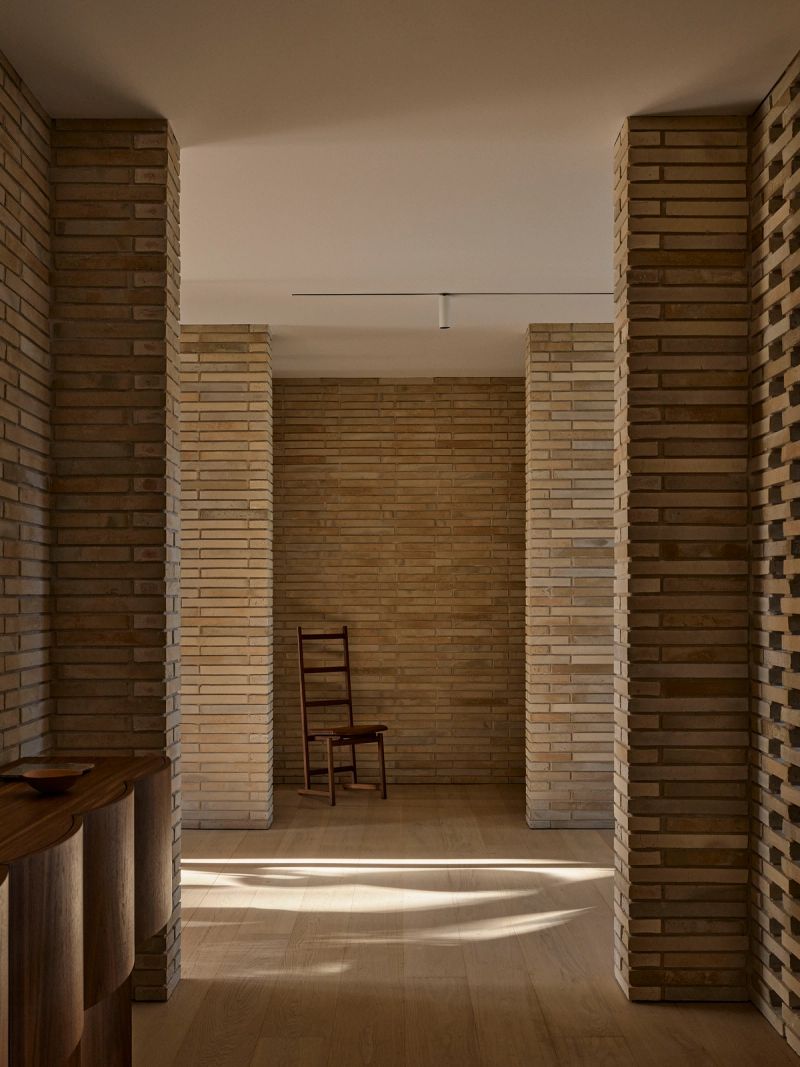 Brick hallway with a timber chair at the far end, lit from the side