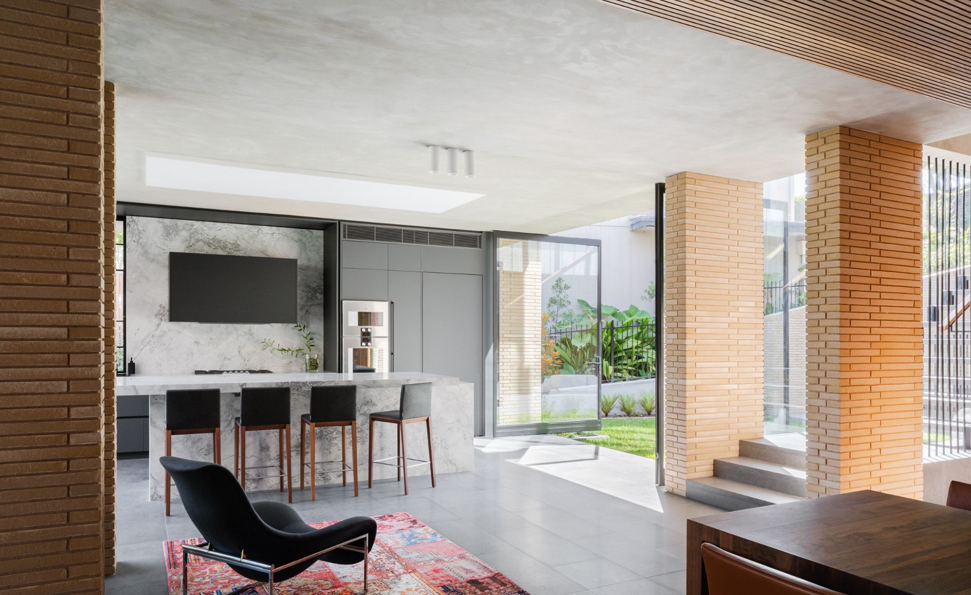 Kitchen and living room with a marble island, brick columns and a red rug