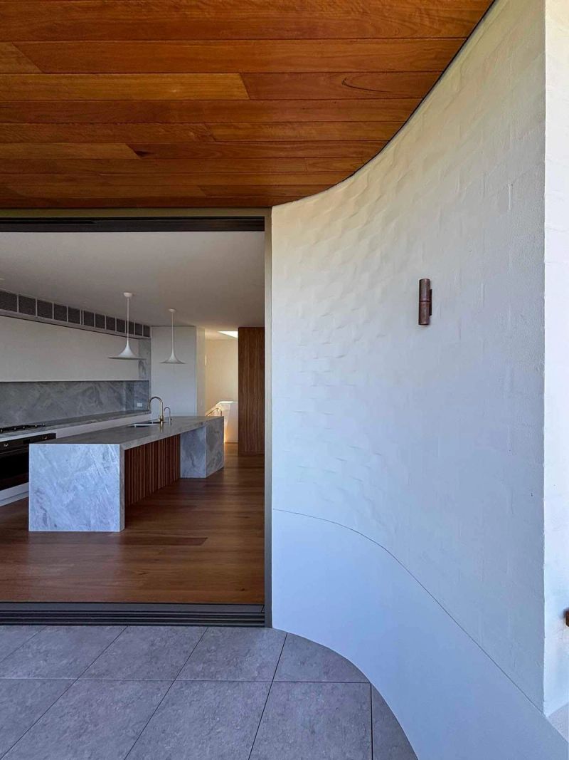 Curved white textured wall beside the kitchen, under a timber ceiling