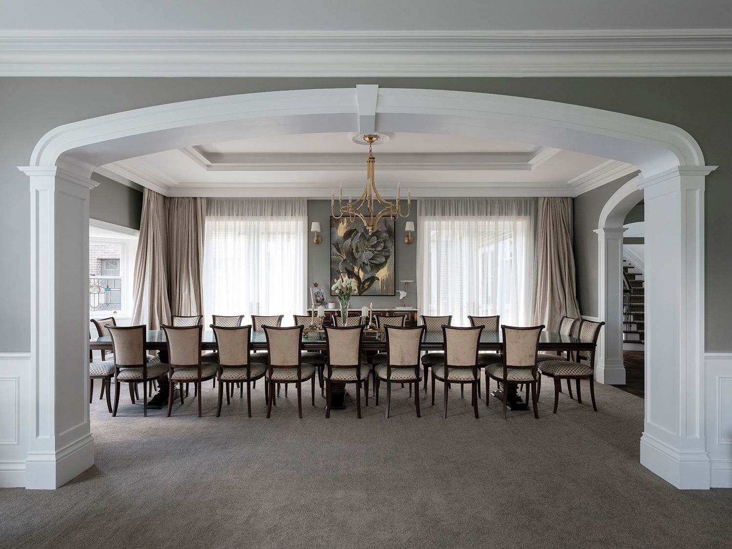 Formal dining room with a long table under a chandelier, framed by arches