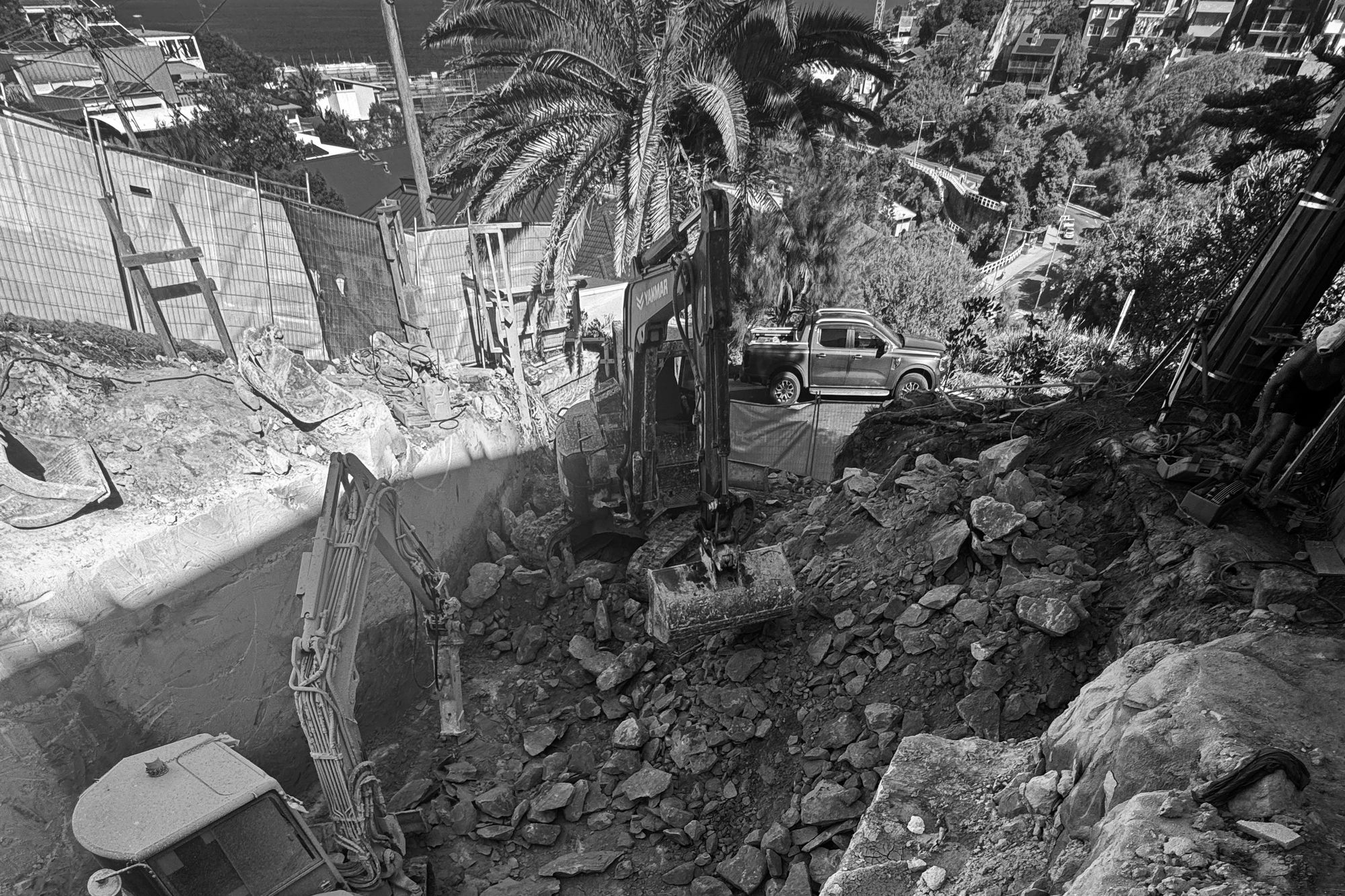 Excavation on the steep site at Tamarama, an excavator below the street with the ocean beyond