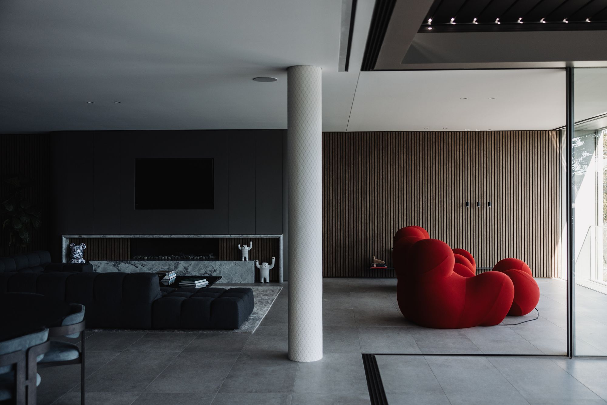 Shellbank living room with timber battened walls, a red sculptural armchair and a round column