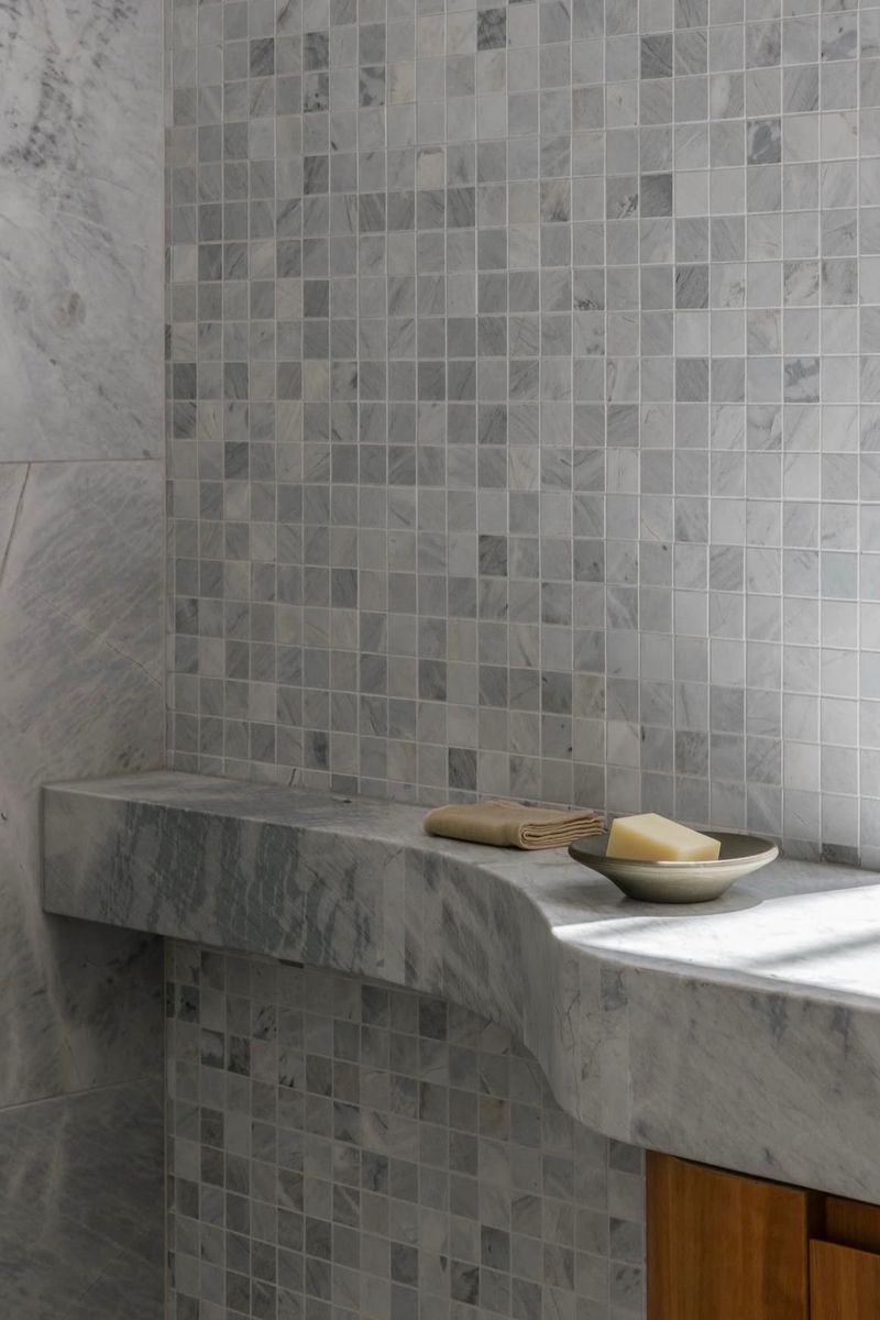 Marble mosaic shower wall with a stone shelf holding soap