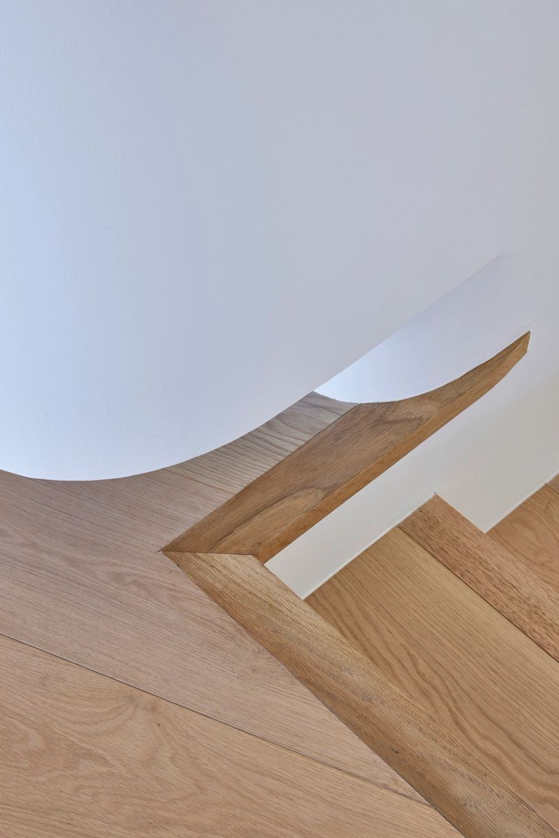 Detail of the timber staircase where the treads meet a curved white wall
