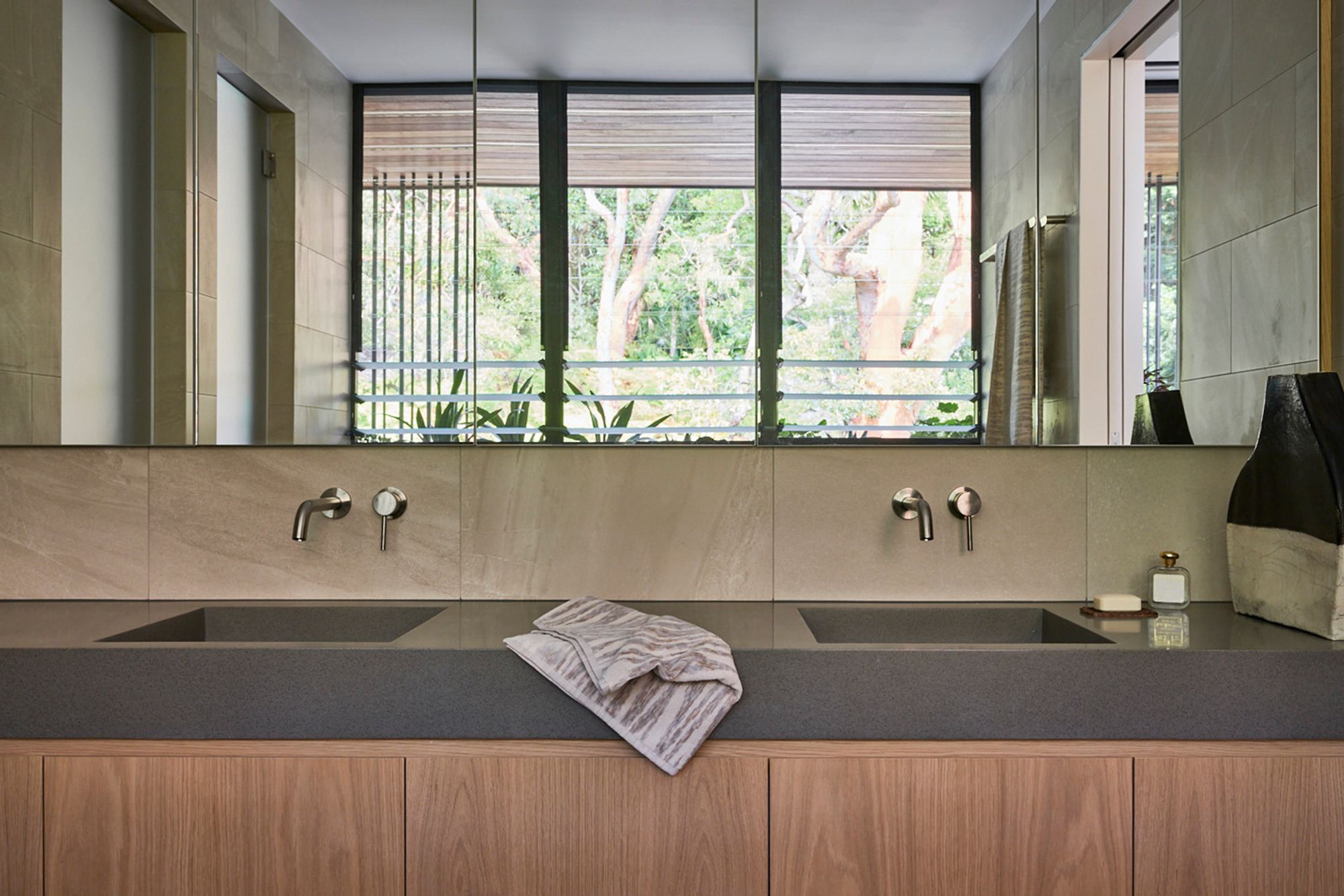 Bathroom with a double stone basin and a mirror reflecting the trees