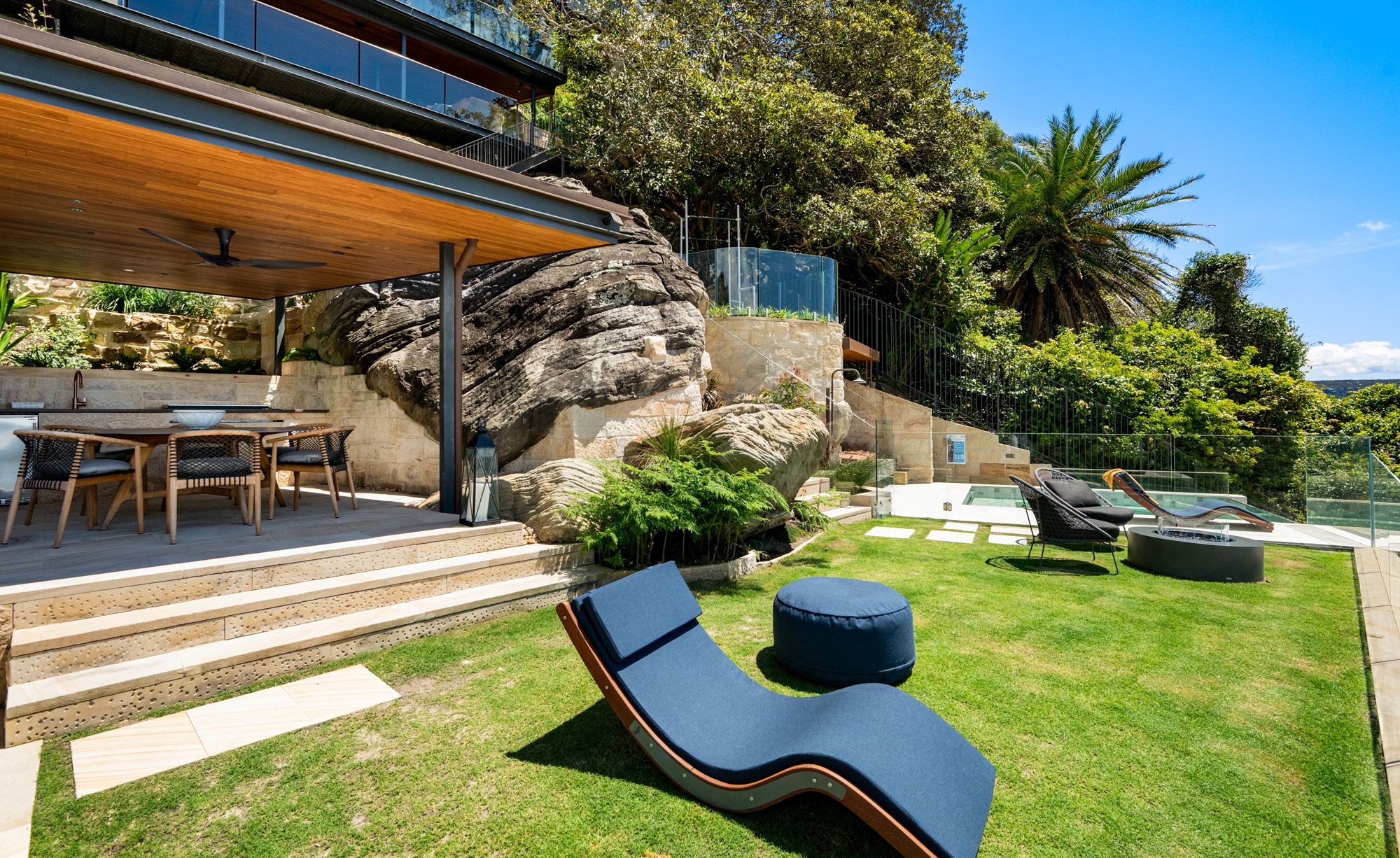 Lawn terrace with a lounger, outdoor dining and a sandstone outcrop