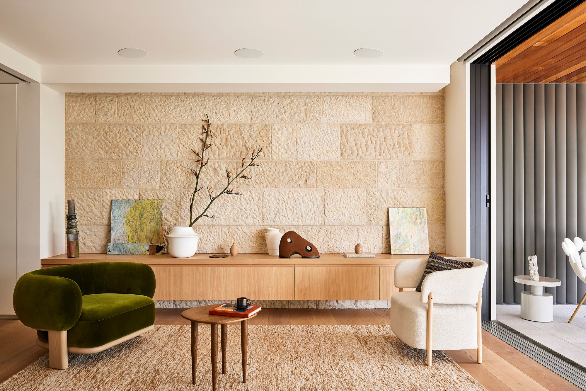 Cobbittee House living room with a sandstone wall, timber sideboard and a green velvet armchair