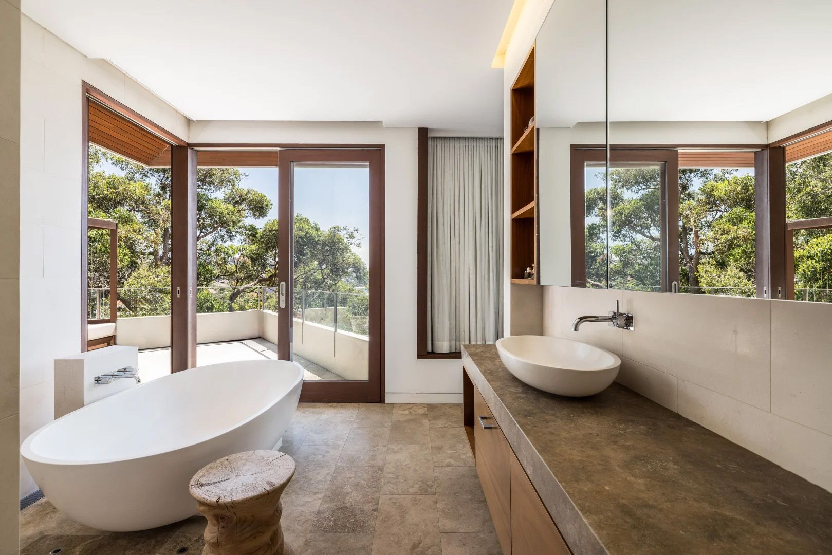 Bathroom with a freestanding bath and a stone vanity, timber framed windows to the trees