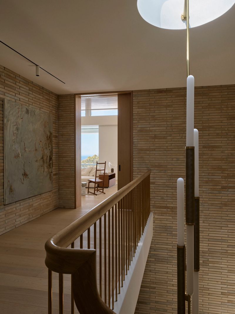 Upper landing with a brass balustrade, pendant lights and a brick wall, looking into a bedroom