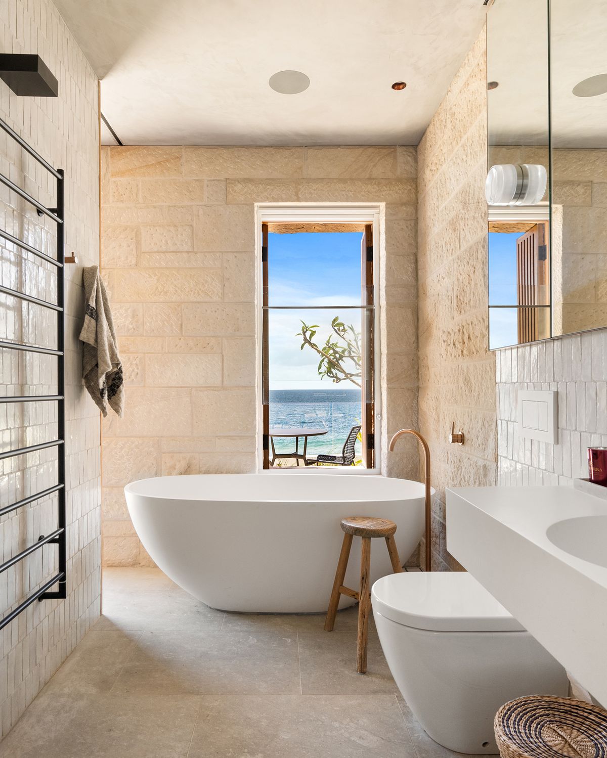 Sandstone bathroom with a freestanding bath and a window to the ocean