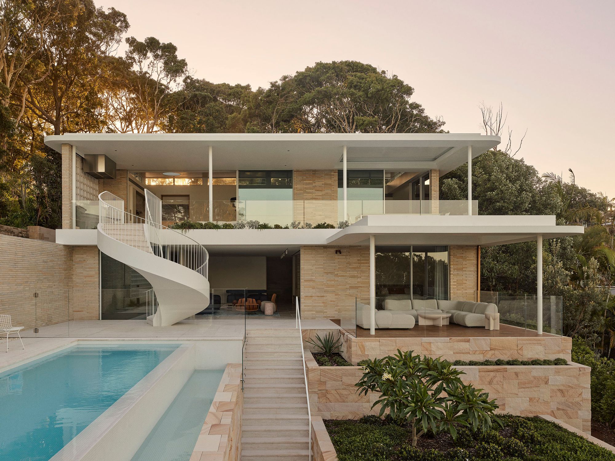 Breeze House from the pool, its two storeys and spiral stair in evening light