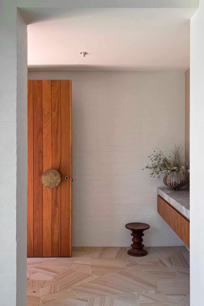 Timber door with a round brass handle beside a white brick wall