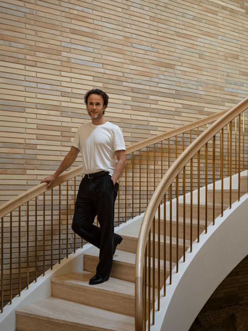 Curved staircase at Breeze House with a brass balustrade and brick wall, a man standing on the steps