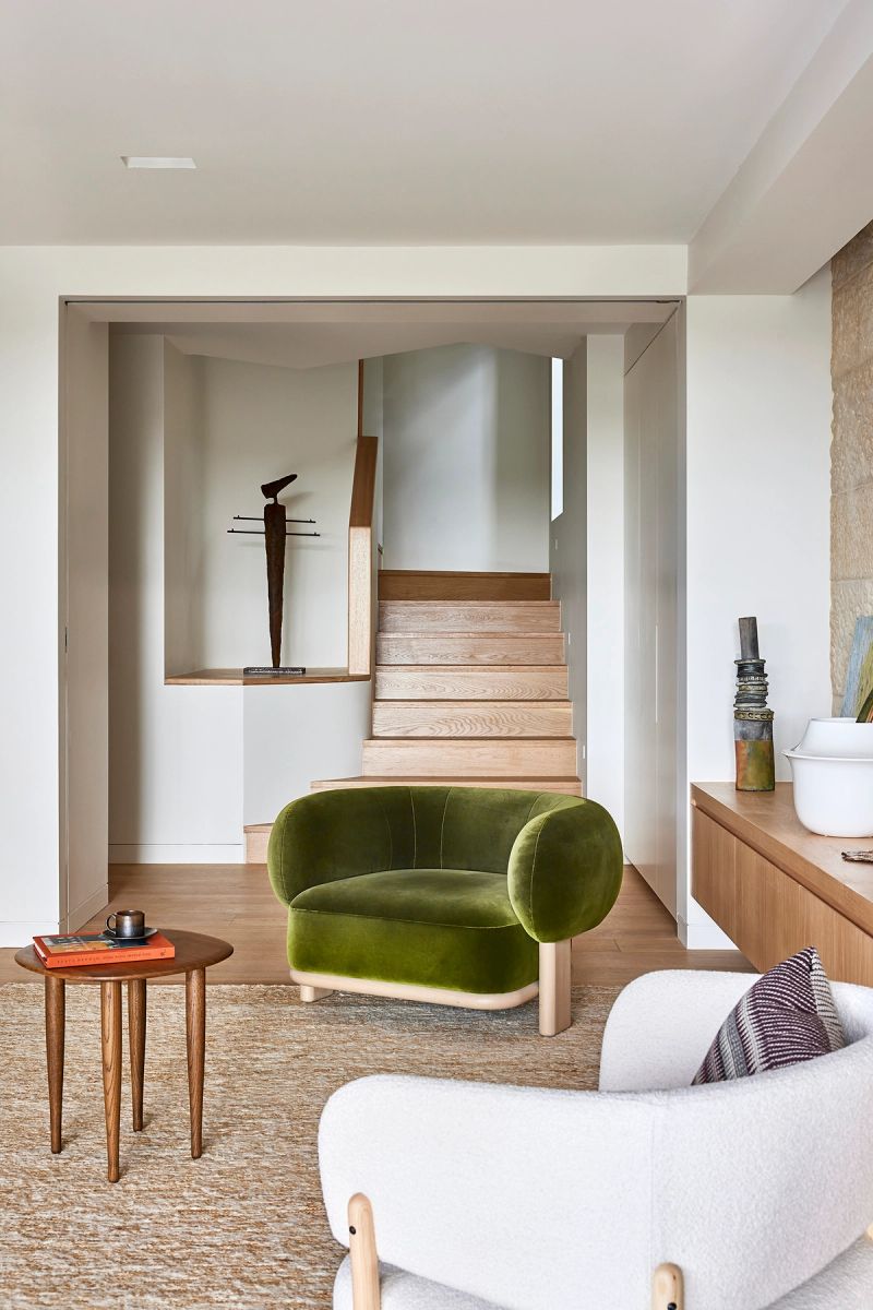 Sitting room with a green velvet armchair and a view up the timber stair