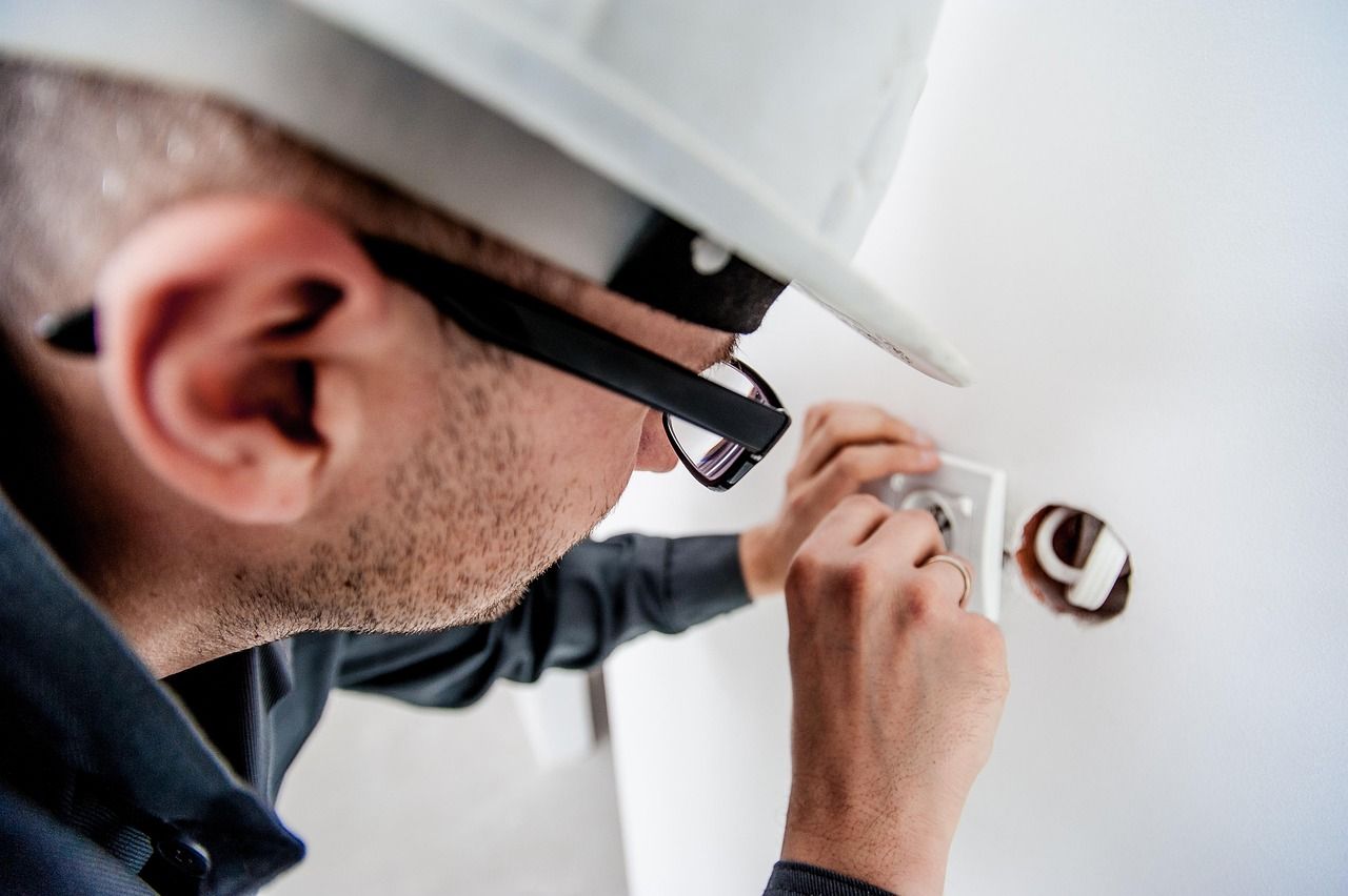 Électricien en casque de sécurité réparant une prise électrique murale