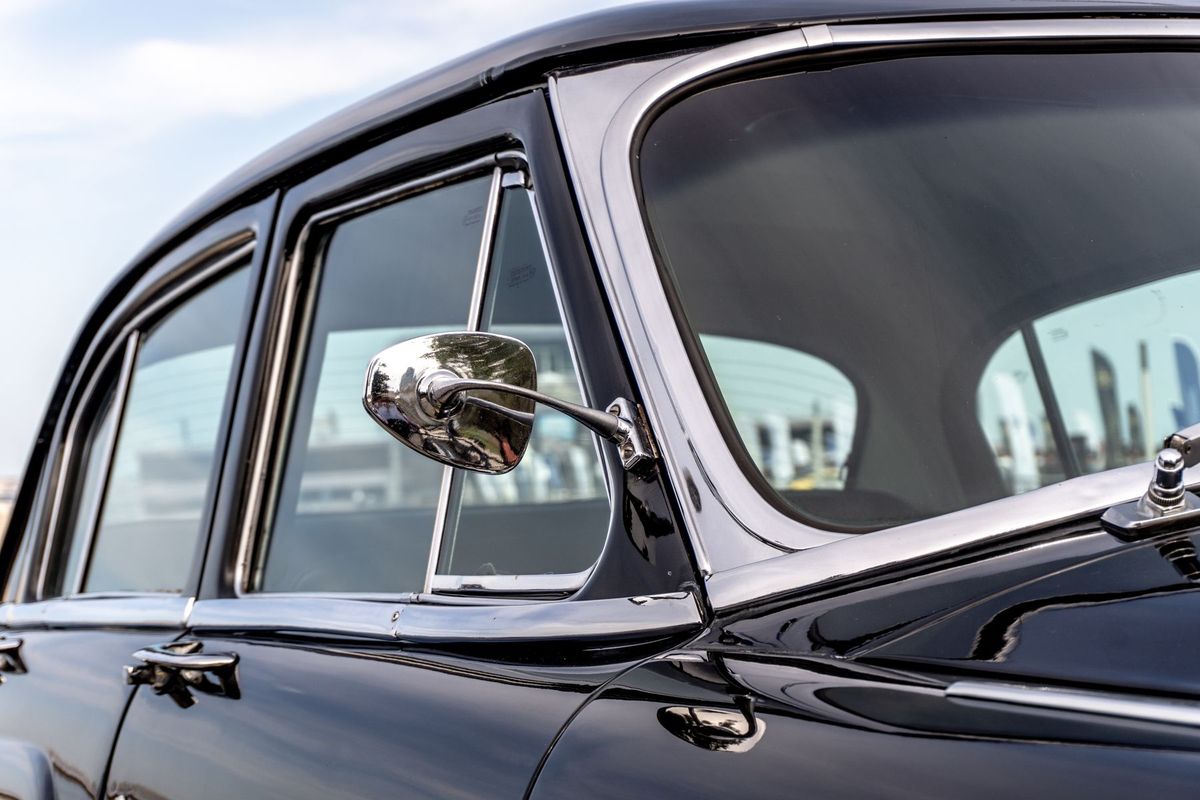 Rétroviseur latéral chromé d'une voiture ancienne reflétant la route