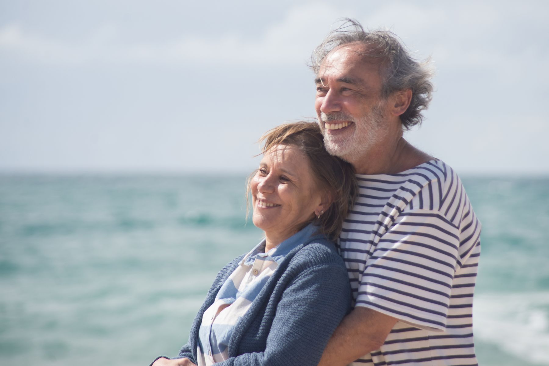 Couple de seniors enlacés face à l'océan sous le soleil, symbolisant une retraite sereine et heureuse