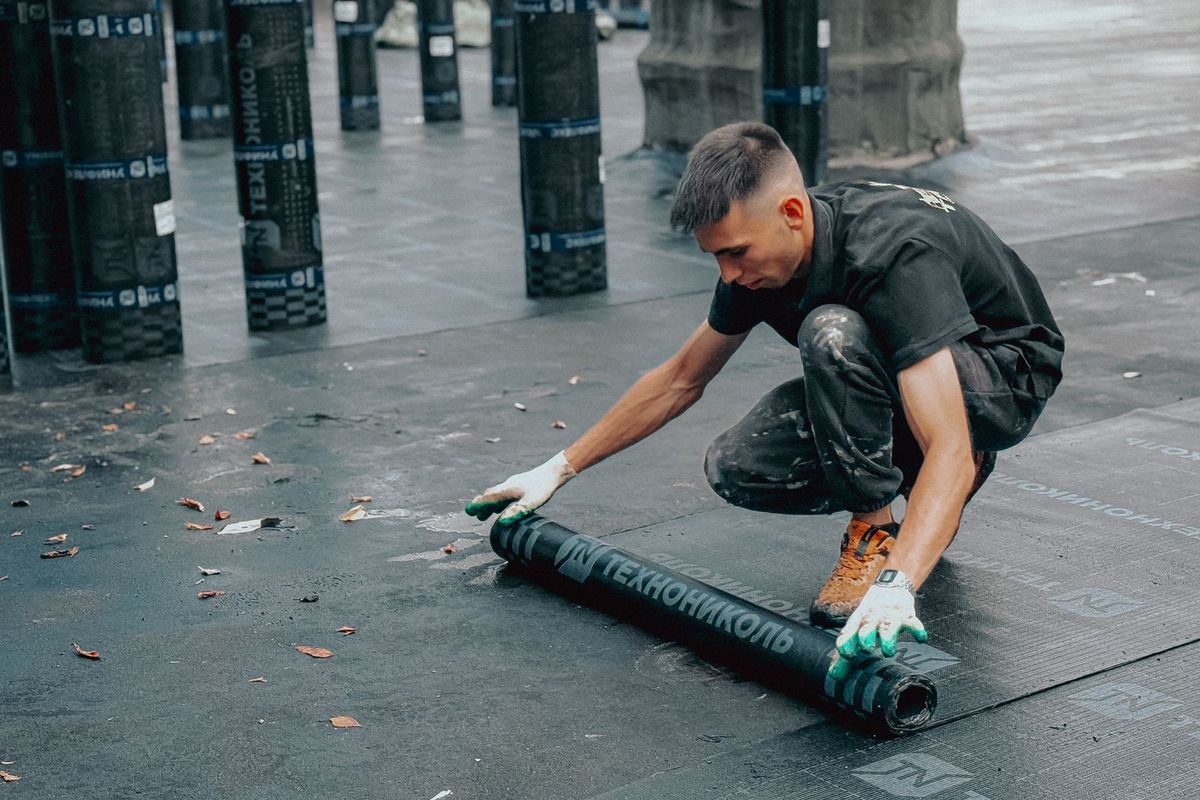 Ouvrier appliquant une membrane d'étanchéité sur un toit en pente
