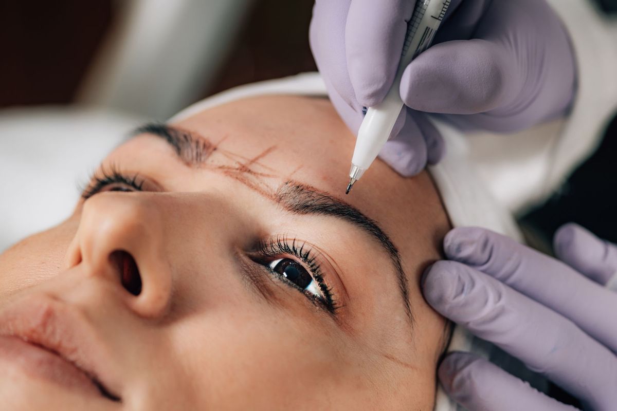Esthéticienne appliquant la technique du microblading sur les sourcils d'une cliente en salon