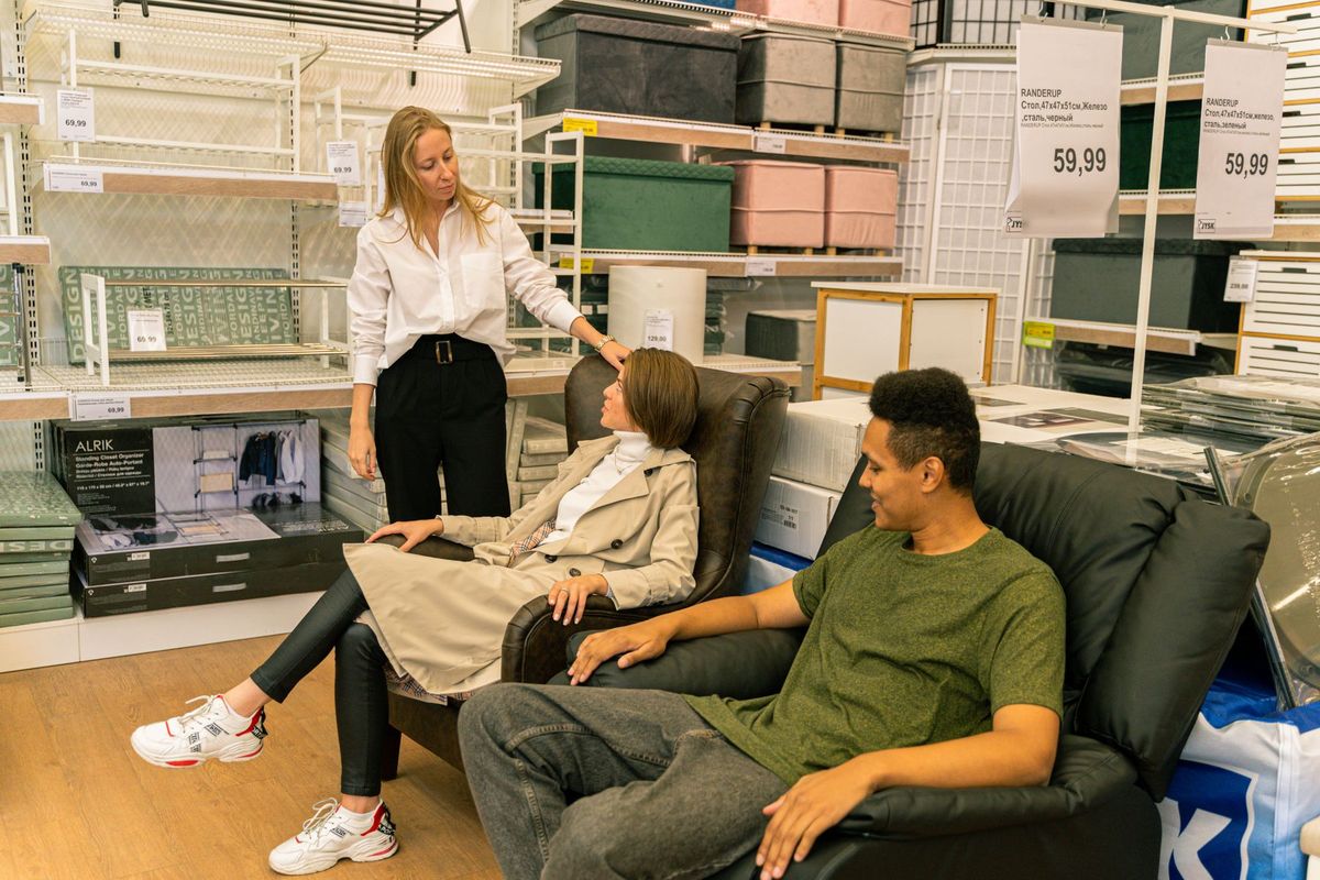 Vendeur conseillant des clients qui testent des fauteuils en cuir dans un showroom de meubles modernes