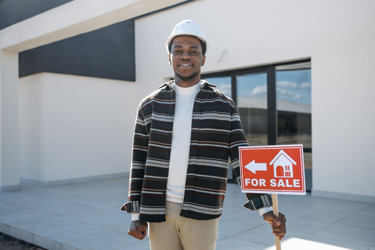 Agent immobilier souriant tenant un panneau À VENDRE devant une maison moderne