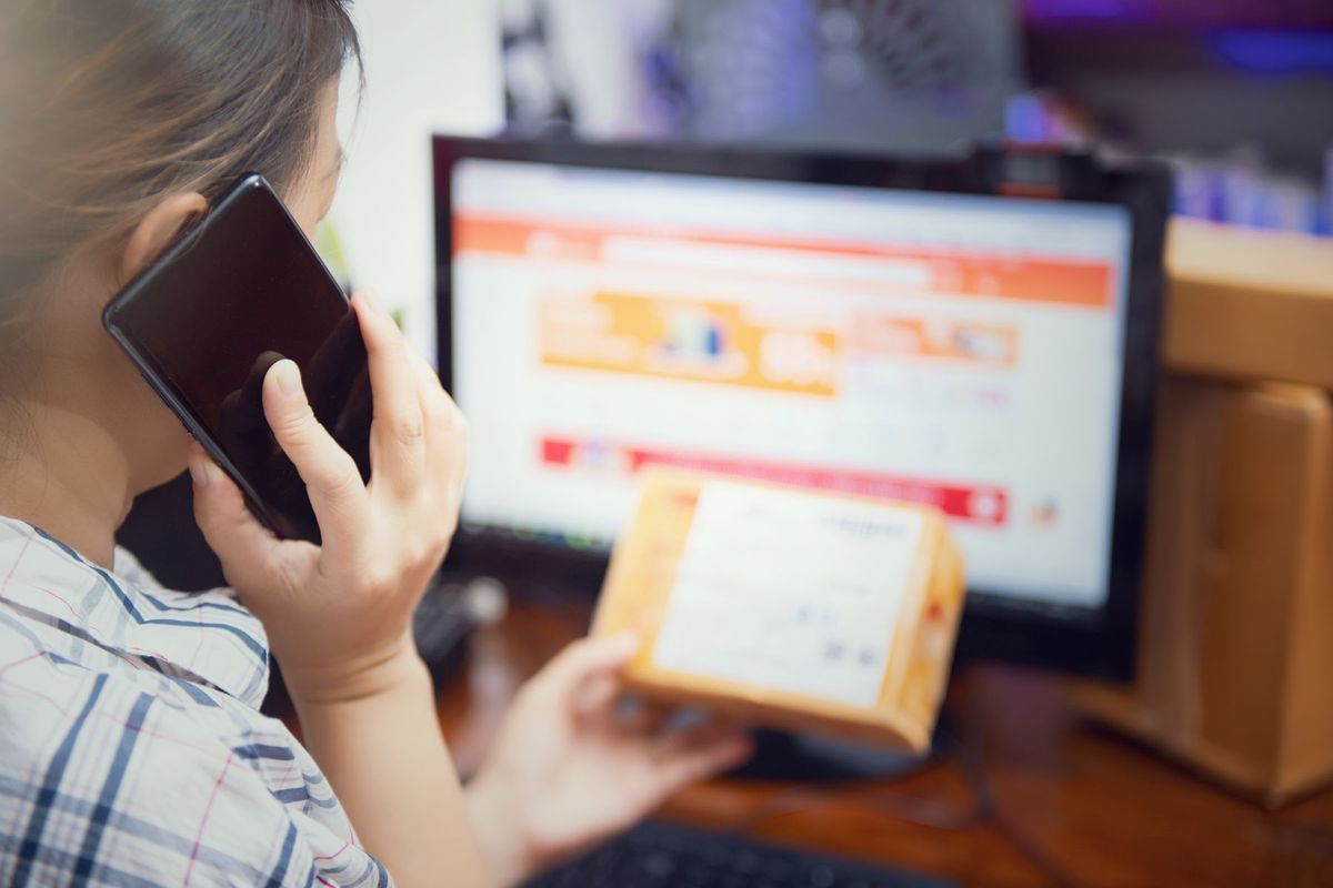 Femme consultant son téléphone tout en inspectant un colis livré à domicile