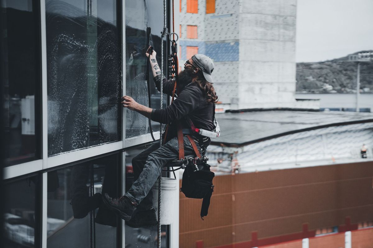 Ouvrier suspendu à un harnais nettoyant les vitres d'une façade de gratte-ciel en milieu urbain