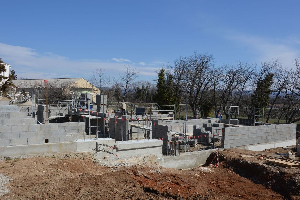 Ouvrier en gilet de sécurité travaillant sur un chantier avec murs en blocs de béton et échafaudages